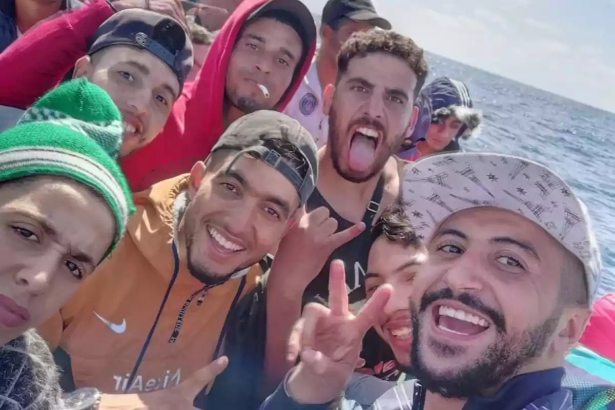 Un grupo de jóvenes ilegales sonríe y posa para una selfie en lo que parece ser una embarcación en el mar, con el cielo despejado de fondo