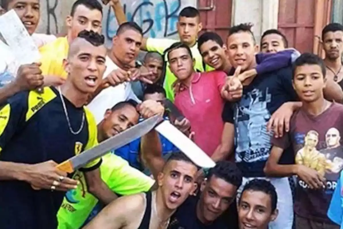 Grupo de jóvenes posando juntos en la calle, algunos de ellos sostienen machetes y cuchillos, todos miran a la cámara con expresiones desafiantes
