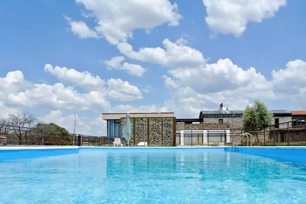 Piscina al aire libre con agua cristalina frente a un edificio moderno bajo un cielo azul con nubes blancas Piscina al aire libre con agua cristalina frente a un edificio moderno bajo un cielo azul con nubes blancas