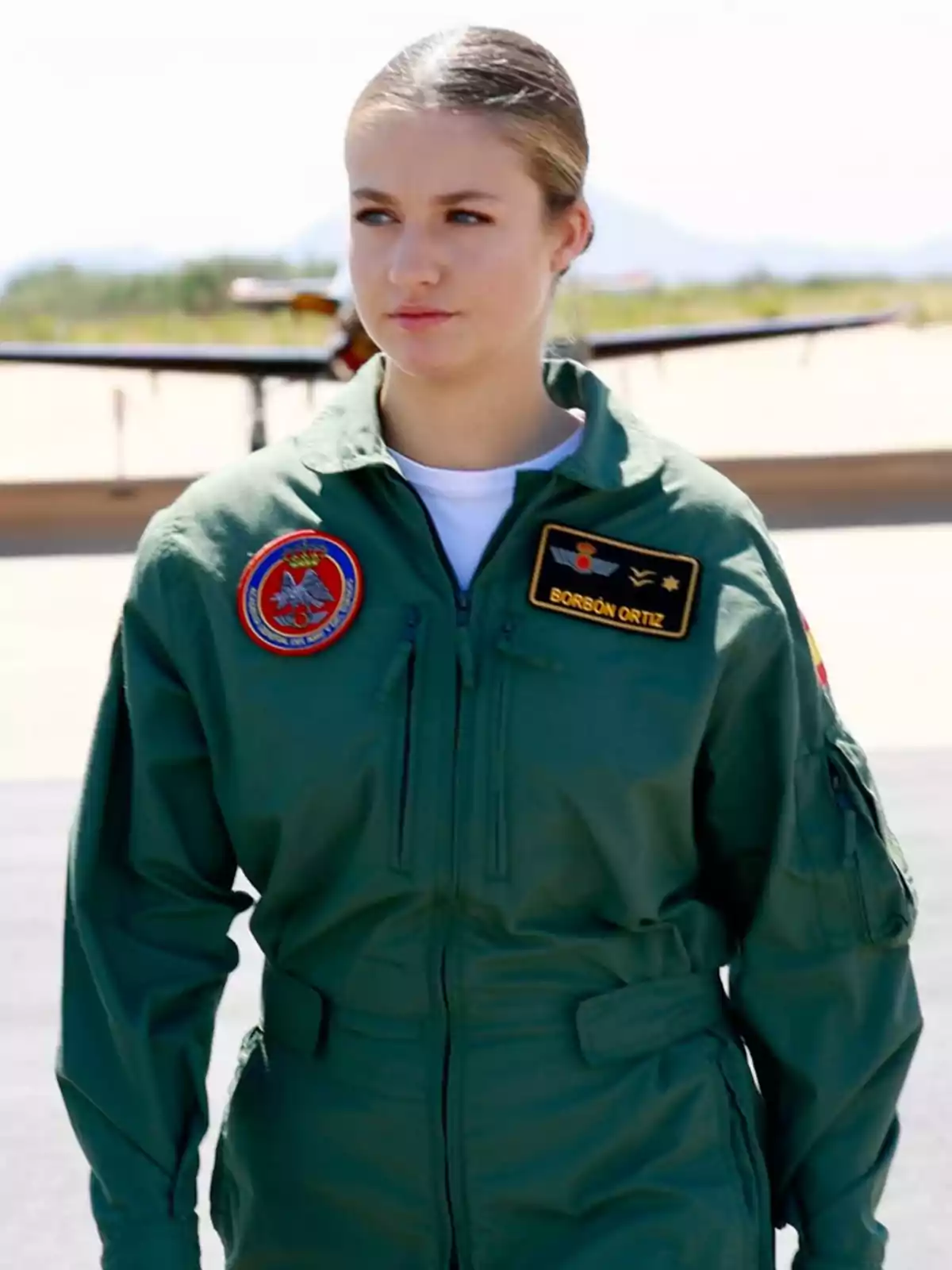 La princesa Leonor vestida con uniforme de piloto militar verde de pie al aire libre con un avión al fondo