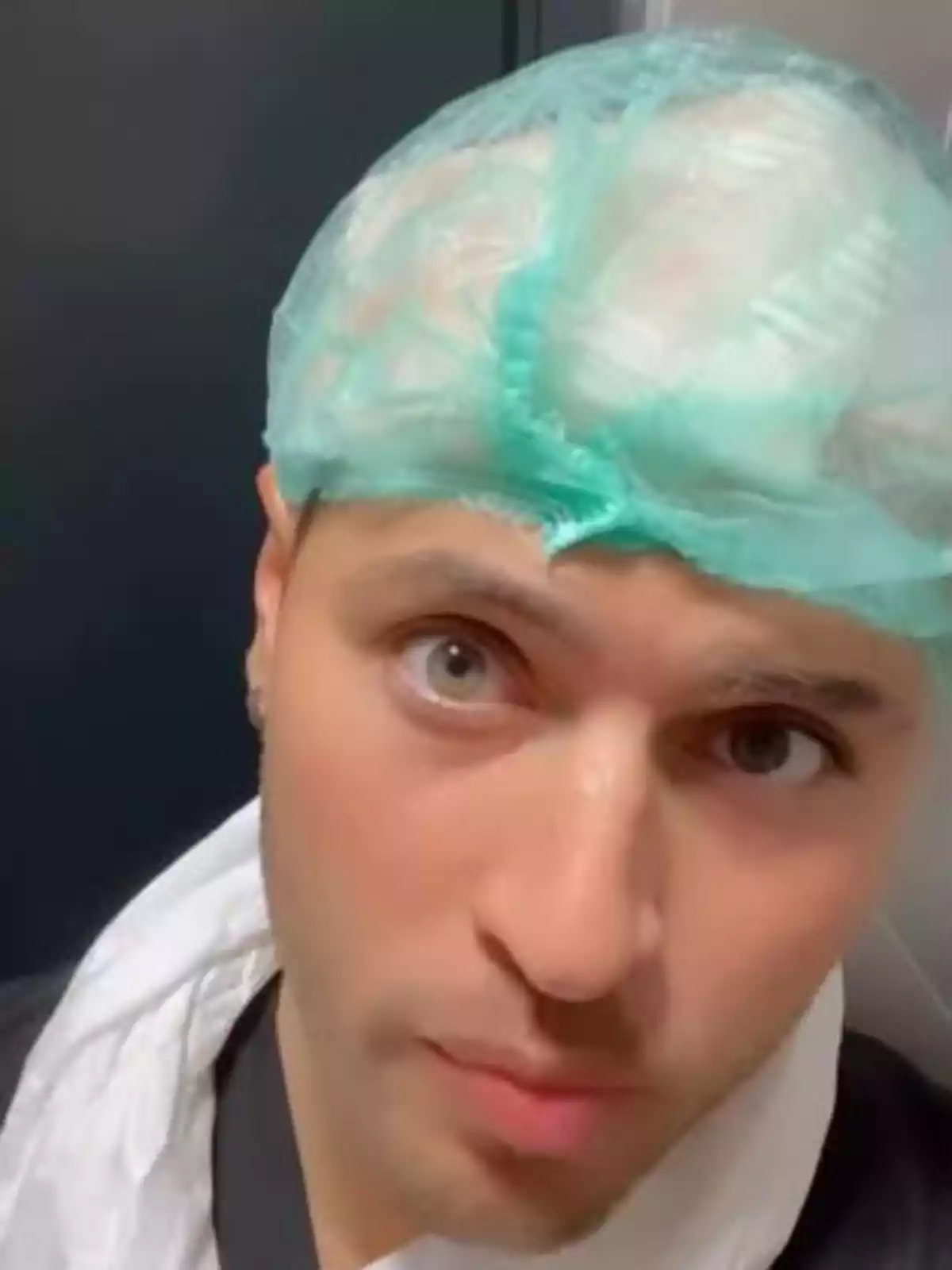 Persona joven con gorro quirúrgico verde y bata blanca mirando a la cámara