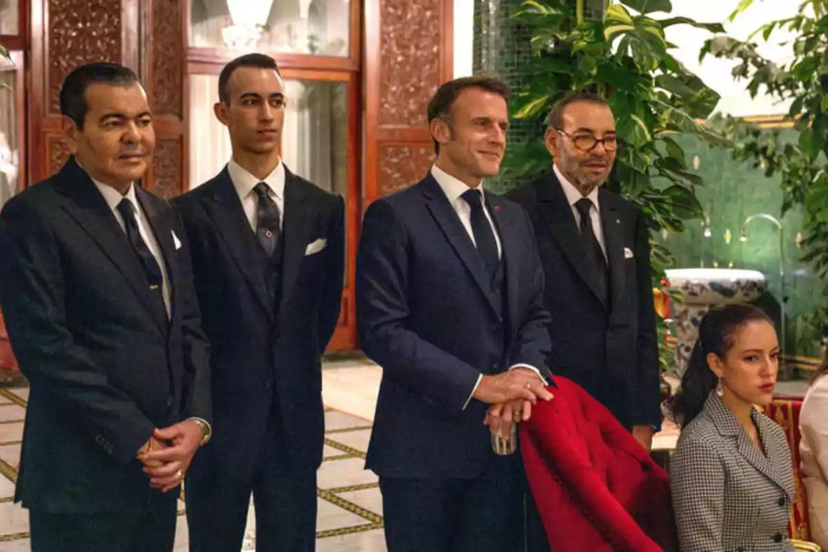 Cinco personas elegantemente vestidas posan en un salón decorado con plantas y detalles de madera tallada Cinco personas elegantemente vestidas posan en un salón decorado con plantas y detalles de madera tallada