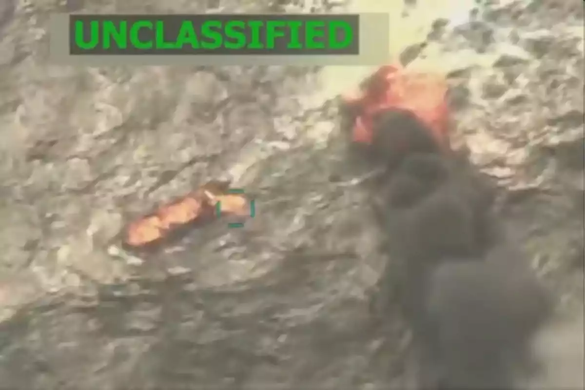 Vista aérea de un terreno rocoso con dos objetos en llamas y humo negro, con la palabra UNCLASSIFIED en la parte superior