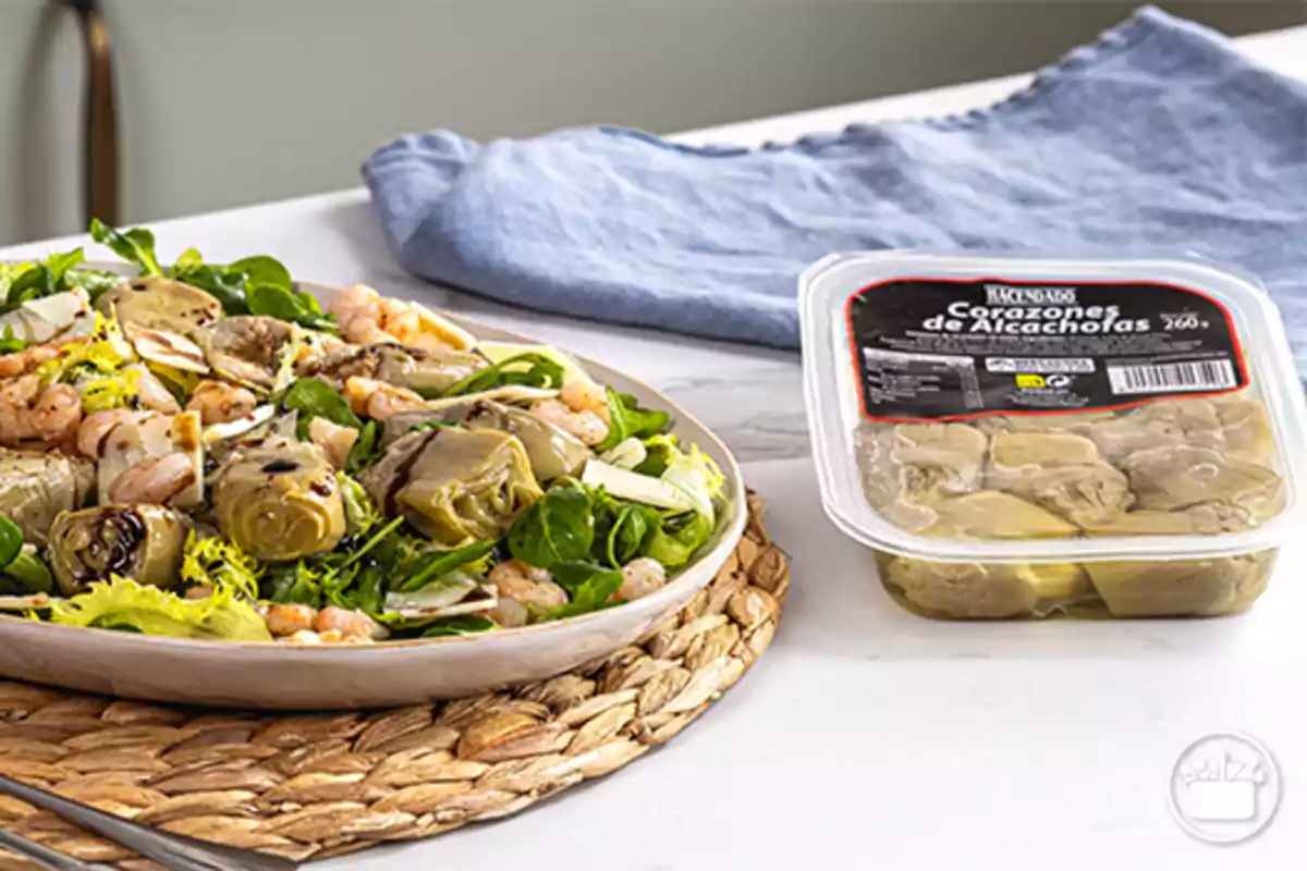 Ensalada de corazones de alcachofa con gambas y queso en un plato junto a un envase de corazones de alcachofa en conserva sobre una mesa blanca