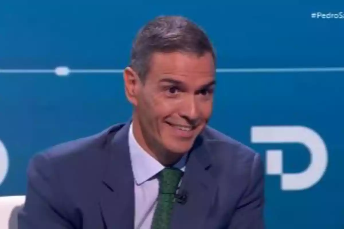 Hombre con traje y corbata verde sonriendo en un plató de televisión con fondo azul Hombre con traje y corbata verde sonriendo en un plató de televisión con fondo azul