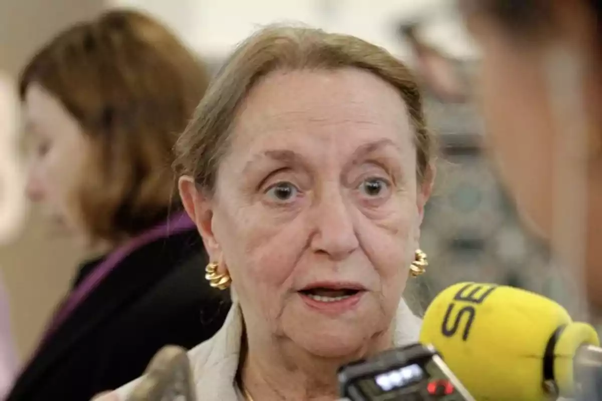 Mujer mayor con expresión de sorpresa siendo entrevistada por varios micrófonos Mujer mayor con expresión de sorpresa siendo entrevistada por varios micrófonos