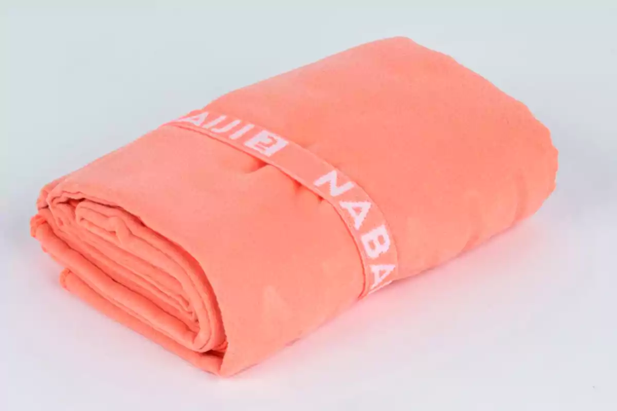Toalla de microfibra color coral enrollada y sujeta con una banda elástica Toalla de microfibra color coral enrollada y sujeta con una banda elástica