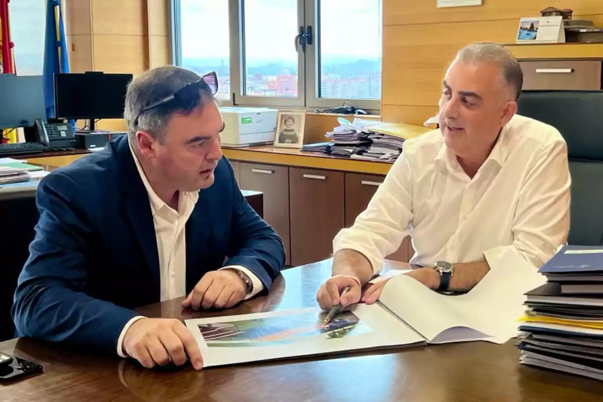 Dos hombres de negocios conversan en una oficina mientras revisan documentos sobre una mesa Dos hombres de negocios conversan en una oficina mientras revisan documentos sobre una mesa