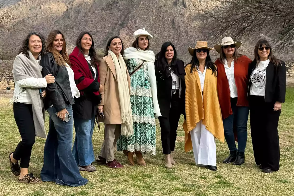 Nueve mujeres posan sonrientes al aire libre con montañas de fondo, vestidas con ropa abrigada y accesorios como sombreros y bufandas Nueve mujeres posan sonrientes al aire libre con montañas de fondo, vestidas con ropa abrigada y accesorios como sombreros y bufandas
