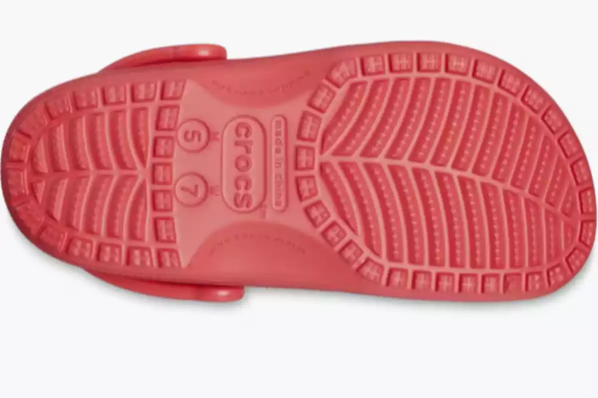 Suela de sandalia Crocs color rosa vista desde abajo mostrando el diseño antideslizante y el nombre de la marca en el centro Suela de sandalia Crocs color rosa vista desde abajo mostrando el diseño antideslizante y el nombre de la marca en el centro