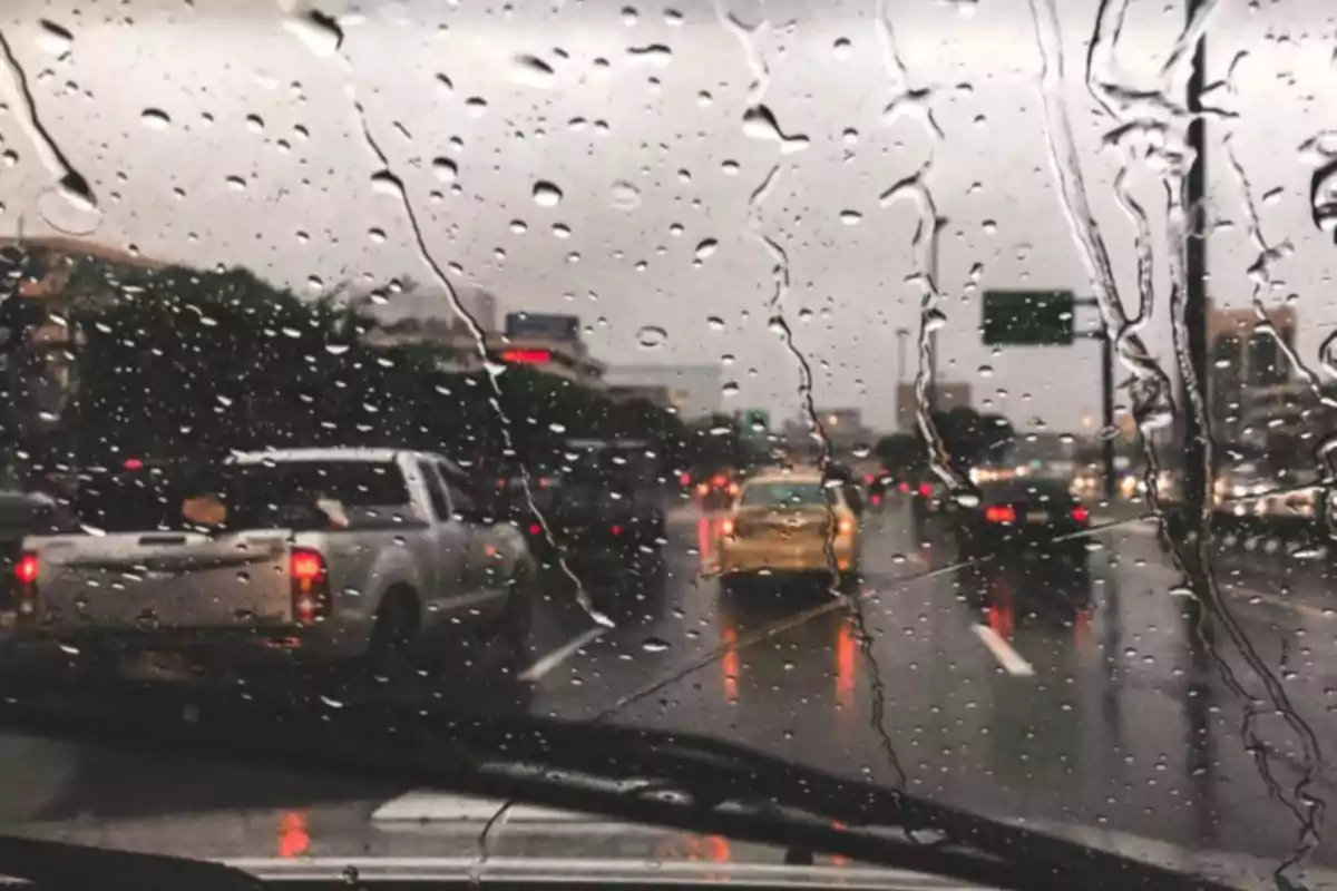 Vista de una calle transitada a través de un parabrisas con gotas de lluvia en un día nublado