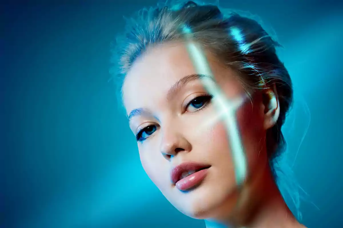 Mujer joven con cabello rubio y piel clara iluminada por luces azules y destellos futuristas sobre su rostro