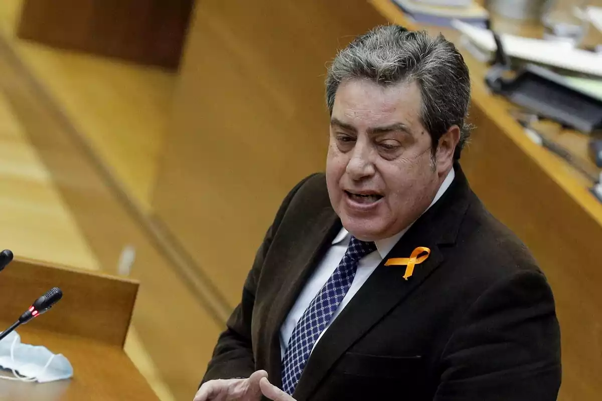 Hombre de cabello canoso hablando en un podio con un lazo naranja en la solapa de su saco Hombre de cabello canoso hablando en un podio con un lazo naranja en la solapa de su saco