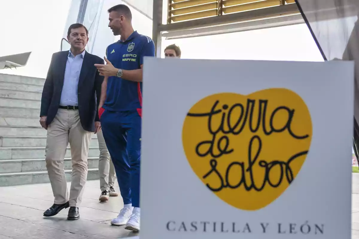 Dos hombres conversan mientras caminan junto a un cartel de Tierra de Sabor Castilla y León