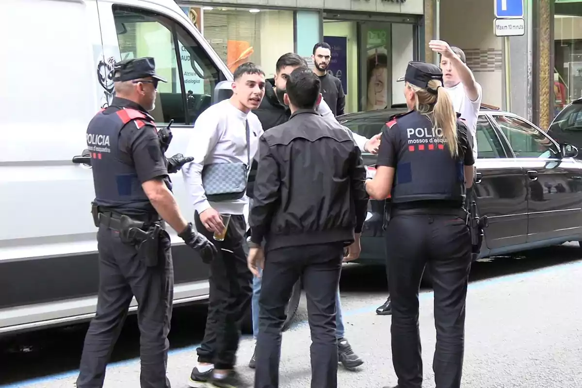 Varios agentes de policía dialogan con un grupo de personas en la calle junto a una furgoneta blanca y un coche negro.