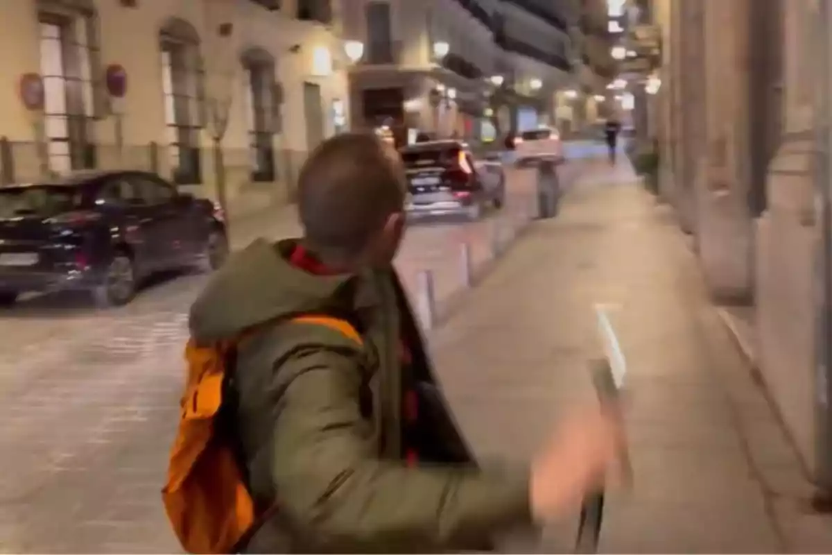 Persona con mochila naranja caminando por una calle iluminada por la noche mientras mira hacia atrás Persona con mochila naranja caminando por una calle iluminada por la noche mientras mira hacia atrás