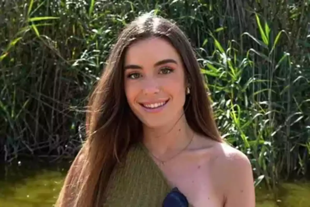 Joven de cabello largo y lacio sonríe al aire libre con vegetación de fondo