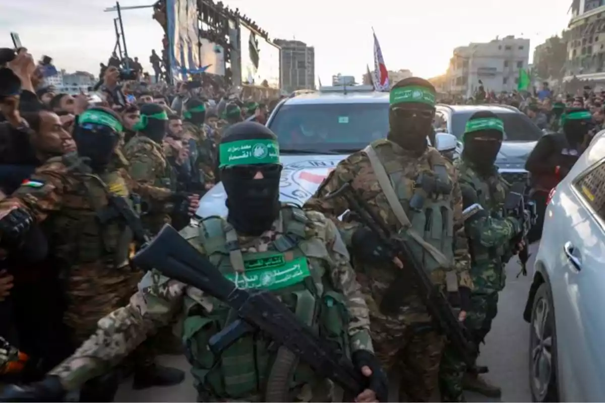 Hombres armados con uniformes de camuflaje y pasamontañas verdes rodeados de una multitud en una calle urbana Hombres armados con uniformes de camuflaje y pasamontañas verdes rodeados de una multitud en una calle urbana