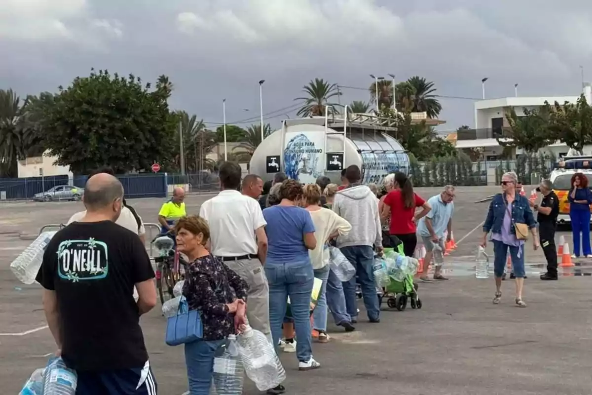 Personas haciendo fila con garrafas vacías para recoger agua de un camión cisterna en un espacio al aire libre Personas haciendo fila con garrafas vacías para recoger agua de un camión cisterna en un espacio al aire libre