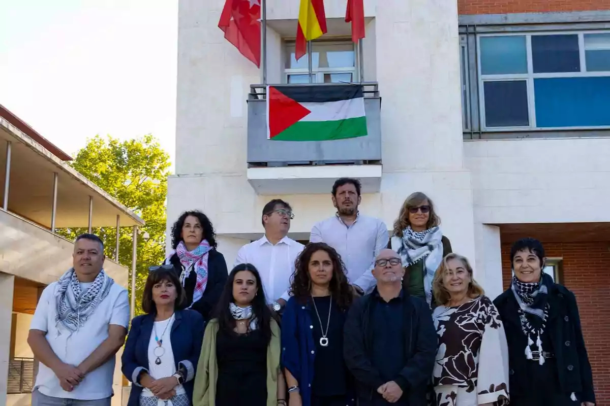 Un grupo de personas posa frente a un edificio con una bandera palestina colgada en el balcón y tres banderas en la parte superior