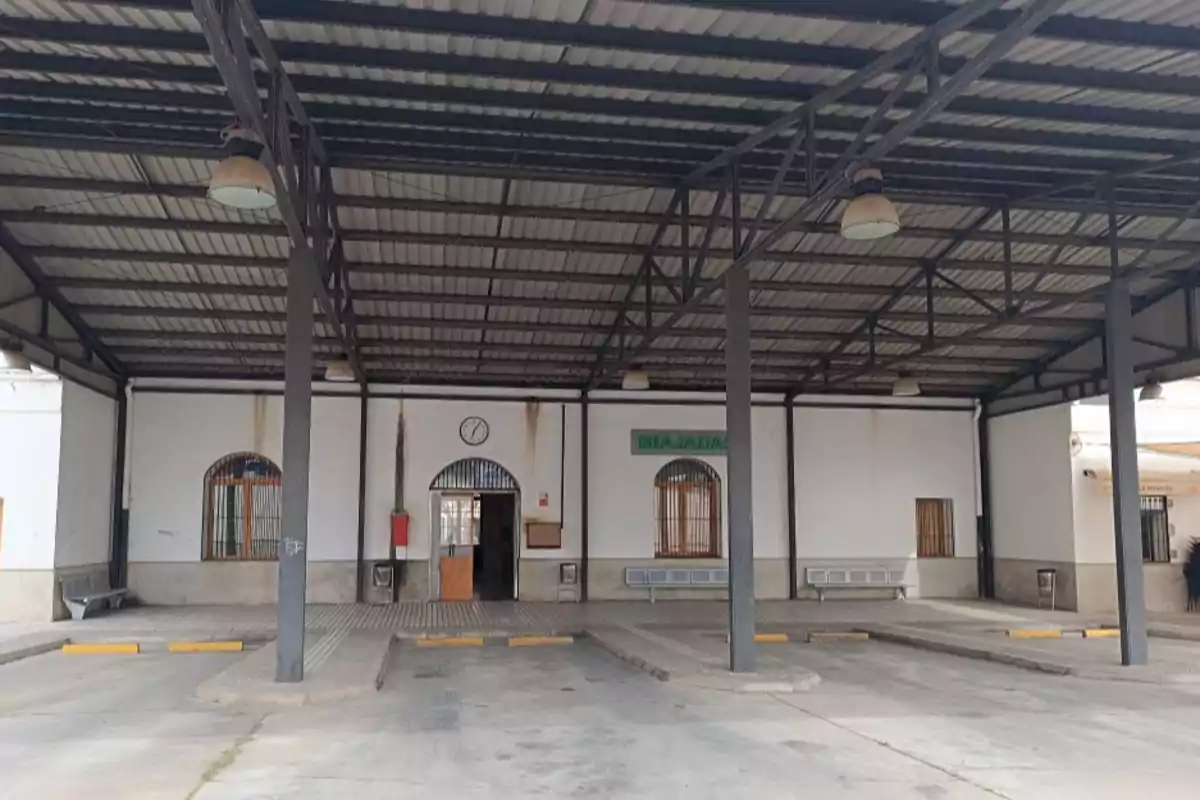 Andén cubierto de una estación de autobuses con bancas metálicas y un reloj en la pared central