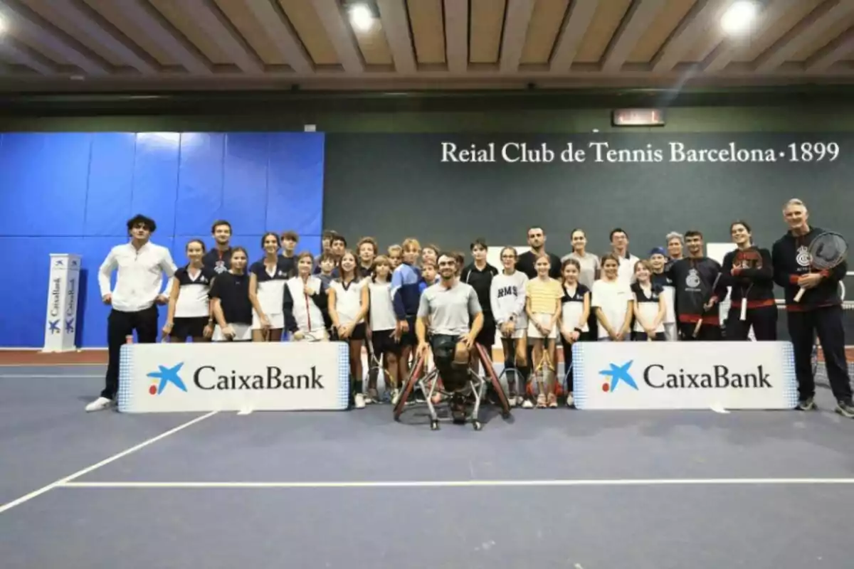 Grupo de personas posando en una cancha de tenis cubierta con raquetas y carteles de CaixaBank en el Reial Club de Tennis Barcelona 1899
