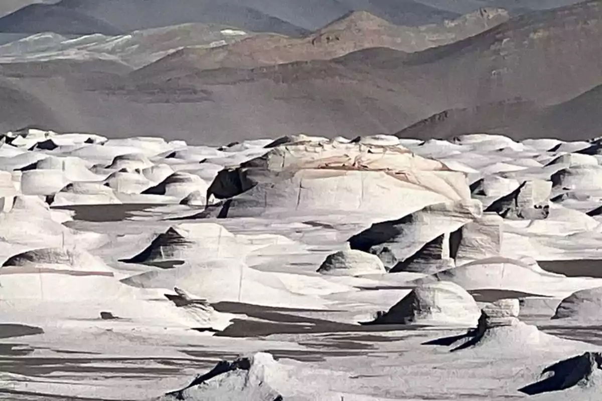 Formaciones rocosas blancas con formas redondeadas en un paisaje desértico rodeado de montañas al fondo Formaciones rocosas blancas con formas redondeadas en un paisaje desértico rodeado de montañas al fondo