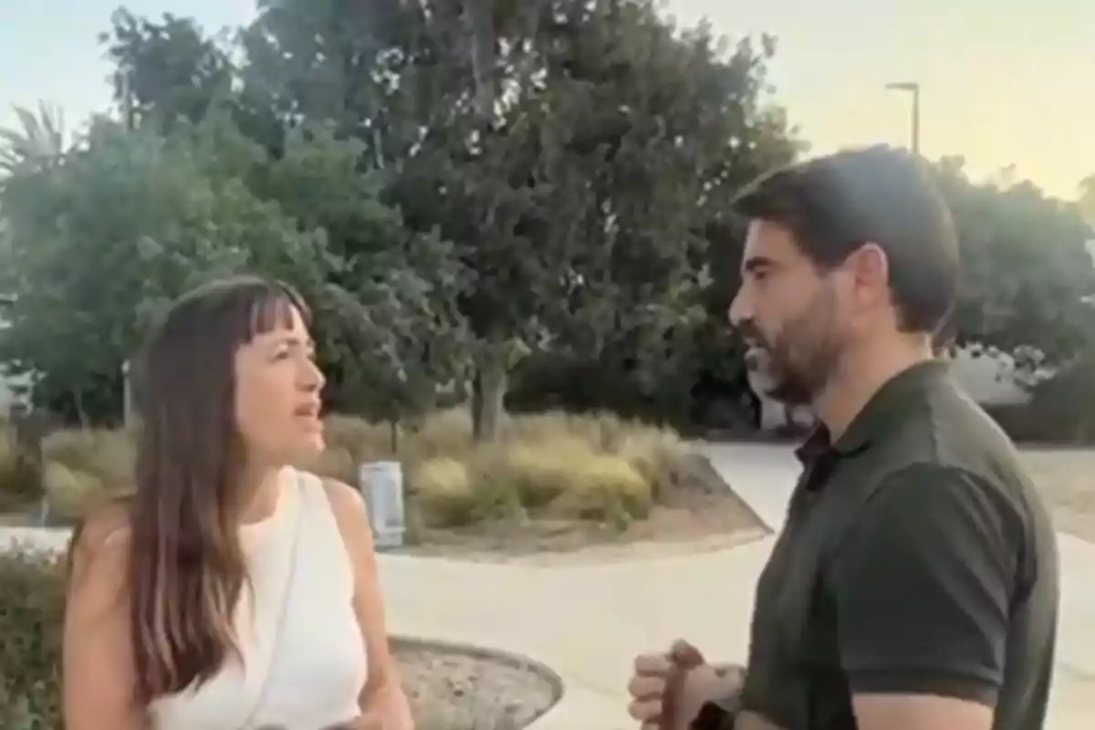 Dos personas conversan al aire libre en un parque con árboles y senderos al fondo Dos personas conversan al aire libre en un parque con árboles y senderos al fondo