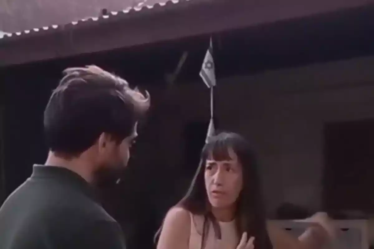 Dos personas conversan frente a una casa mientras una bandera pequeña cuelga en el fondo Dos personas conversan frente a una casa mientras una bandera pequeña cuelga en el fondo