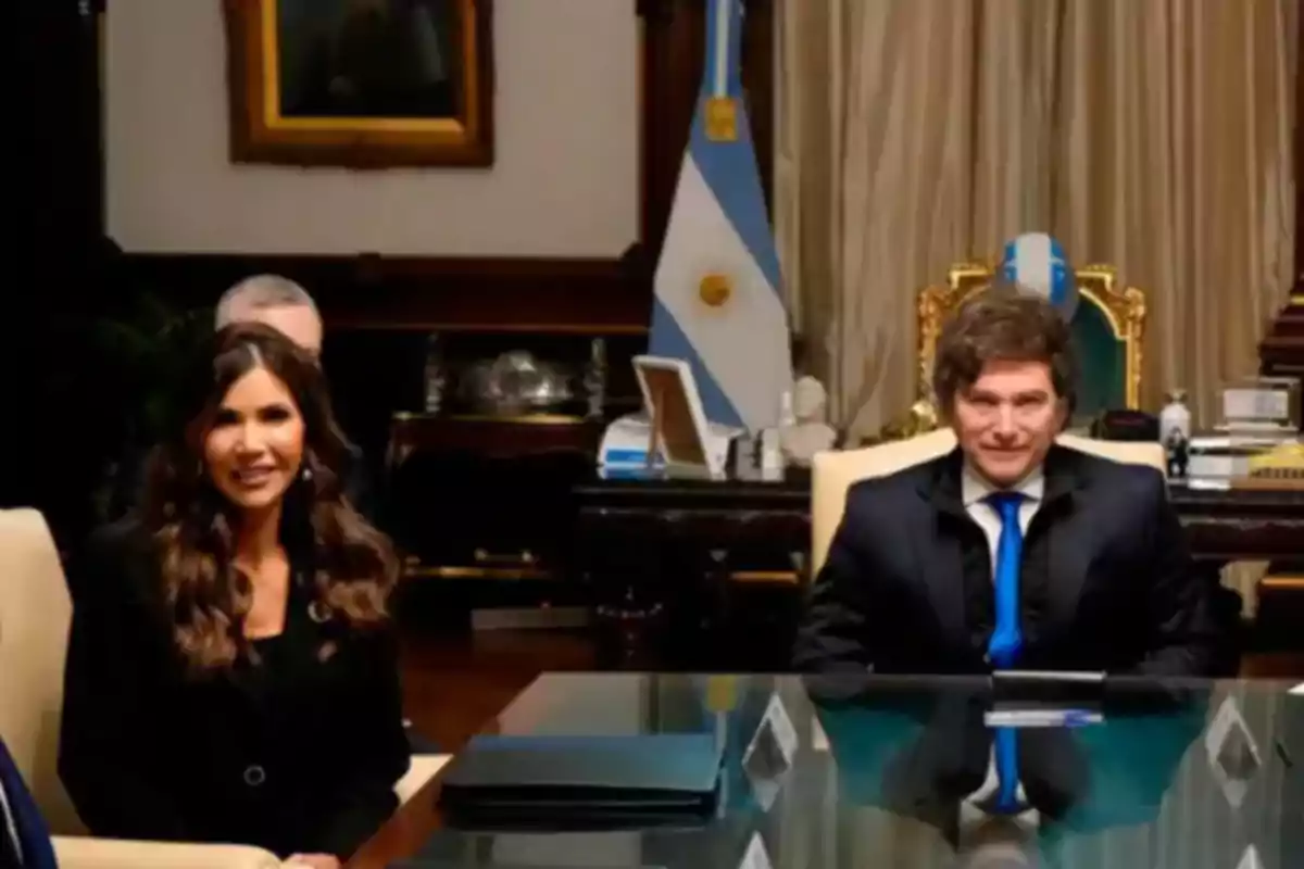 Dos personas sentadas en una mesa de oficina elegante con una bandera de Argentina al fondo