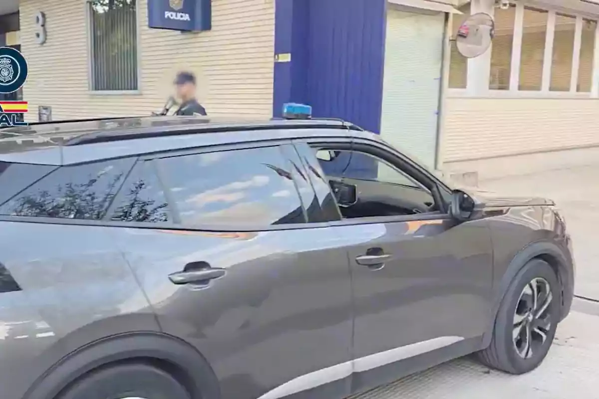 Vehículo gris estacionado frente a una comisaría de policía con un agente al fondo