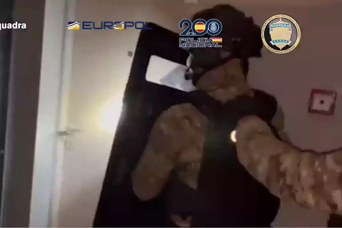 Agente policial con equipo táctico y escudo entrando a una habitación durante un operativo, con logotipos de Europol, Policía Nacional y otras instituciones en la parte superior de la imagen.