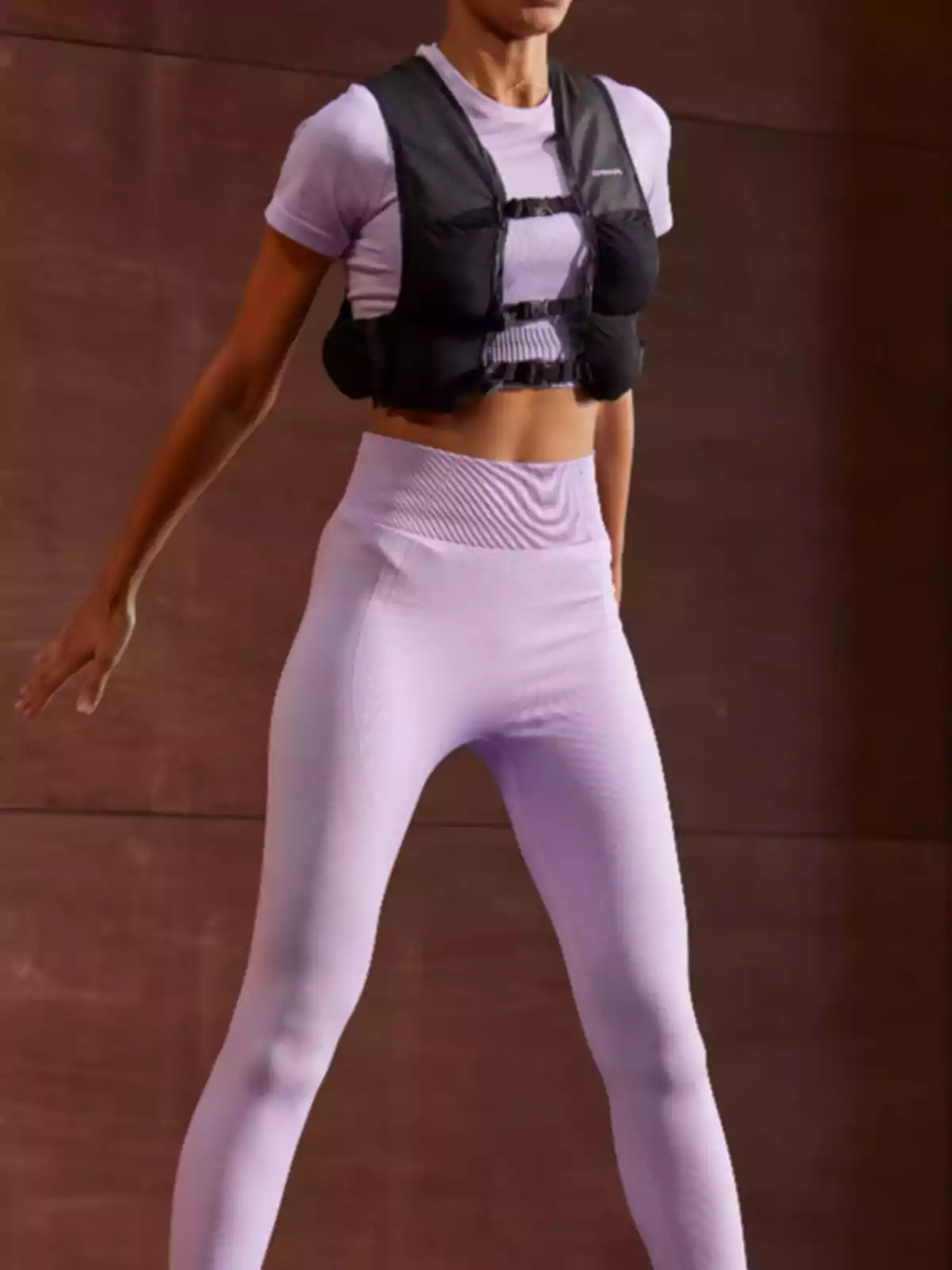 Persona usando ropa deportiva lila y un chaleco de peso negro mientras realiza ejercicio en un espacio interior. Persona usando ropa deportiva lila y un chaleco de peso negro mientras realiza ejercicio en un espacio interior.