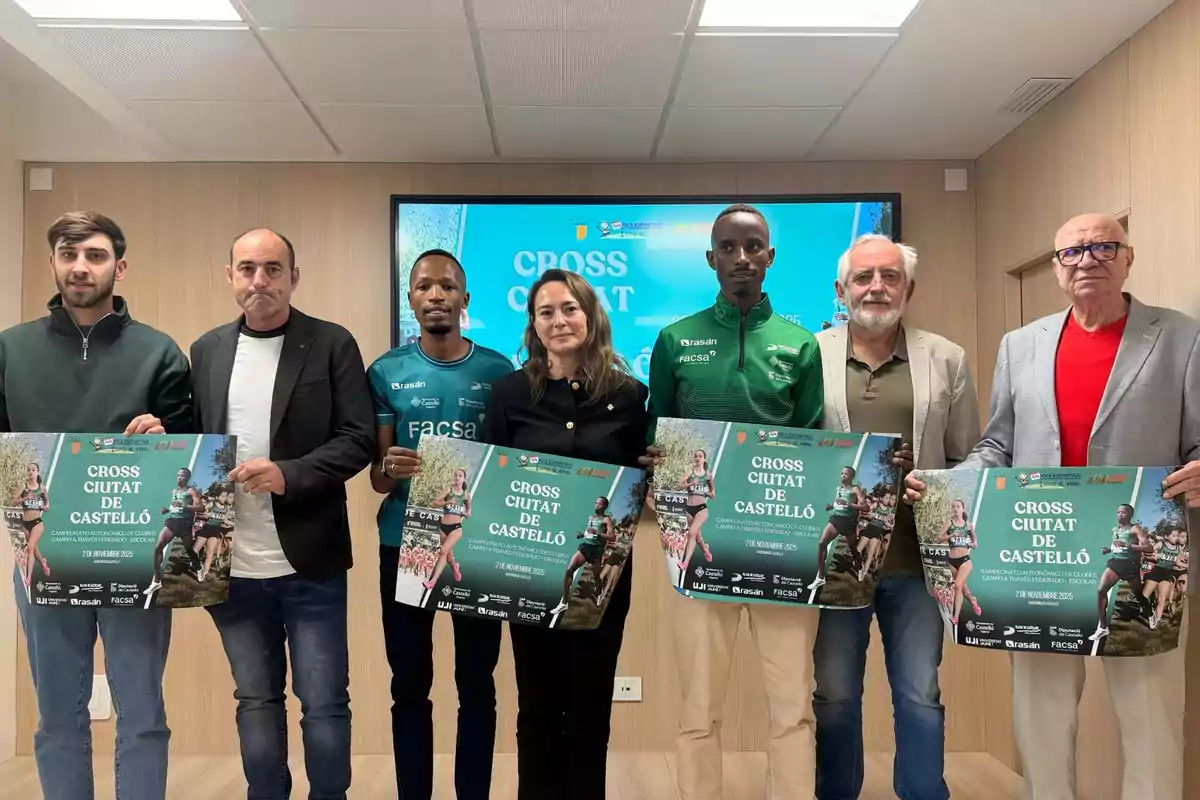 Siete personas posan en una sala sosteniendo carteles promocionales del evento Cross Ciutat de Castelló frente a una pantalla con el mismo anuncio.