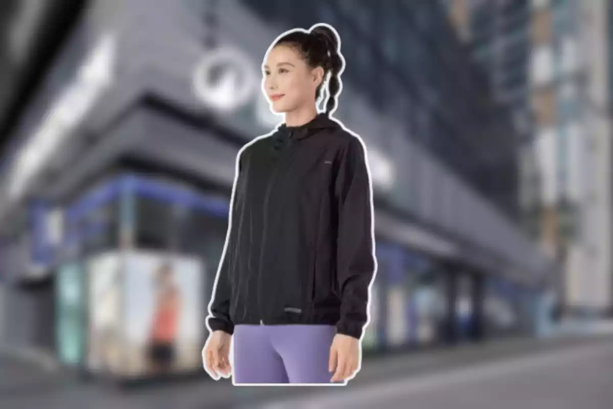 Mujer con chaqueta negra y pantalones deportivos morados de pie frente a un edificio moderno desenfocado