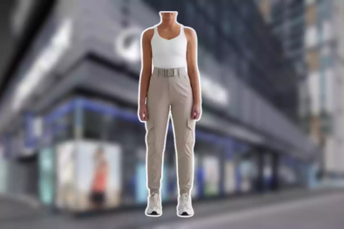 Persona sin cabeza vestida con camiseta blanca y pantalones beige de estilo casual de pie frente a un edificio urbano desenfocado