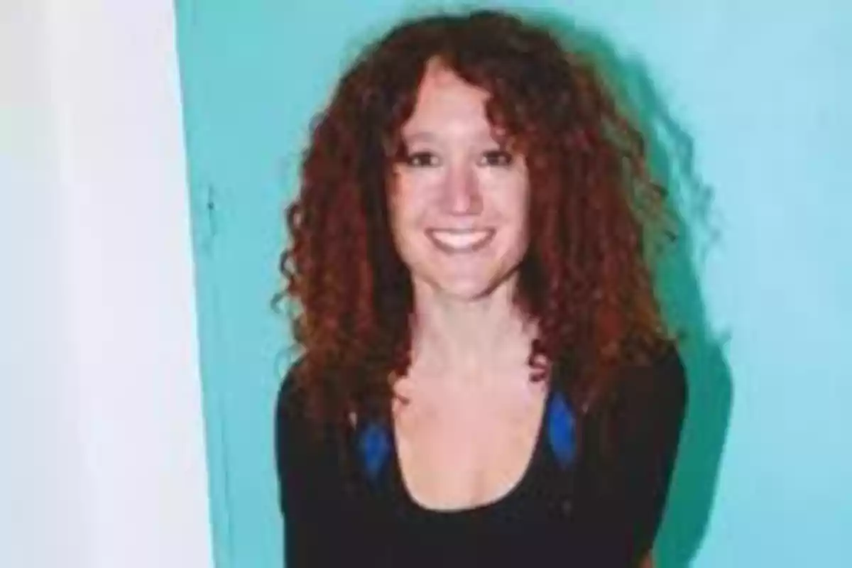 Mujer de cabello rizado y pelirrojo sonriendo frente a una pared azul