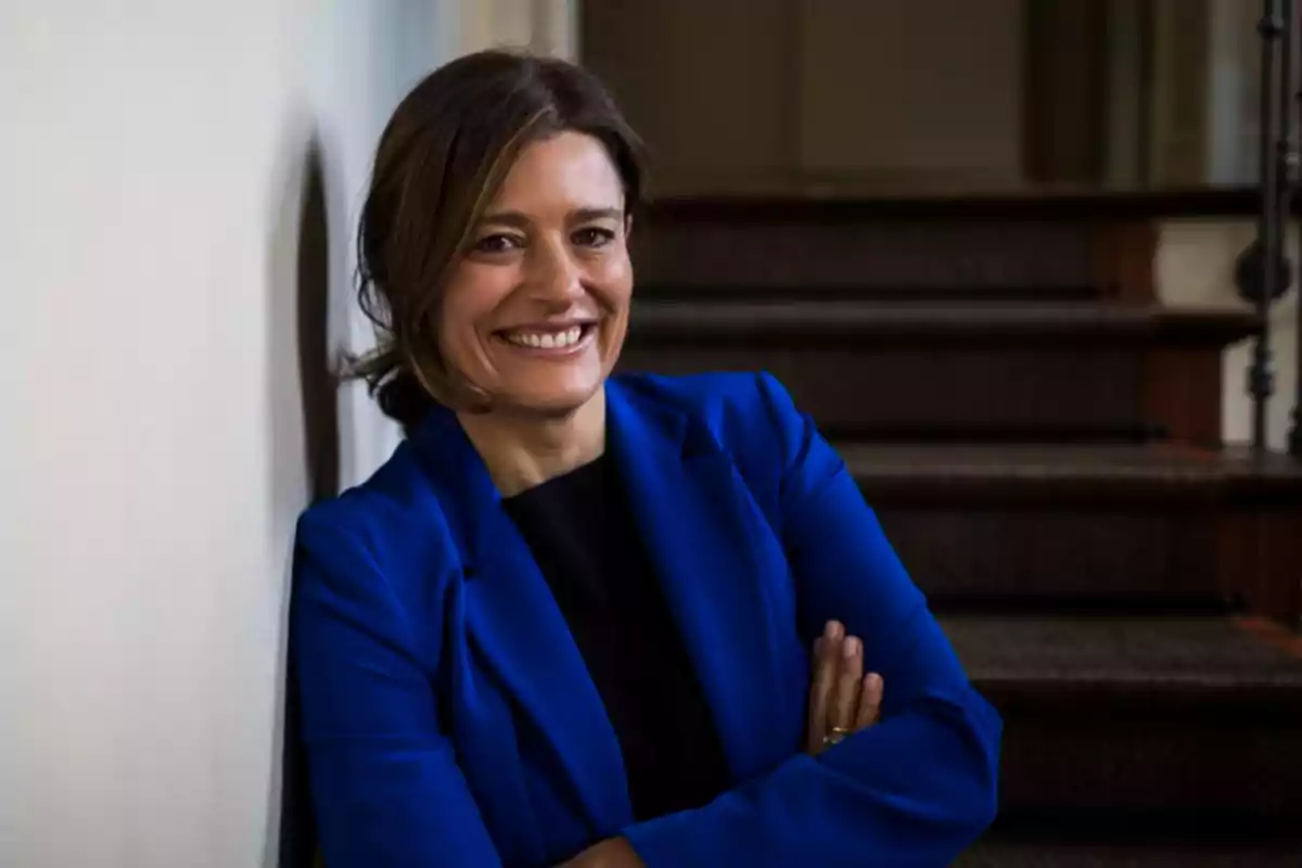 Mujer sonriente con saco azul apoyada en una pared junto a unas escaleras Mujer sonriente con saco azul apoyada en una pared junto a unas escaleras