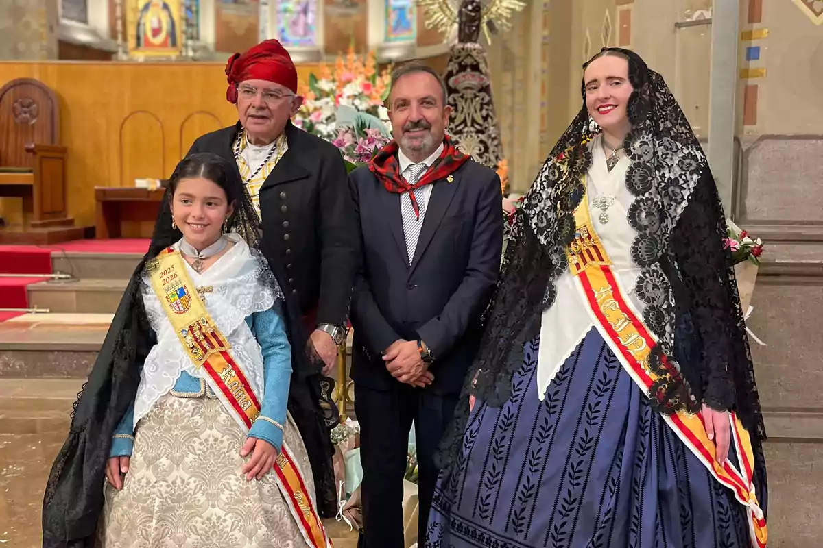 Cuatro personas posan en el interior de una iglesia, dos de ellas llevan trajes tradicionales y bandas con escudos, mientras que las otras dos visten de manera formal y con detalles típicos en el cuello Cuatro personas posan en el interior de una iglesia, dos de ellas llevan trajes tradicionales y bandas con escudos, mientras que las otras dos visten de manera formal y con detalles típicos en el cuello