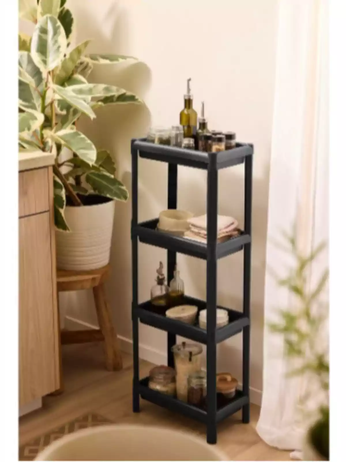 Estante negro de cuatro niveles con frascos y botellas en una esquina junto a una planta grande en maceta y una cortina blanca