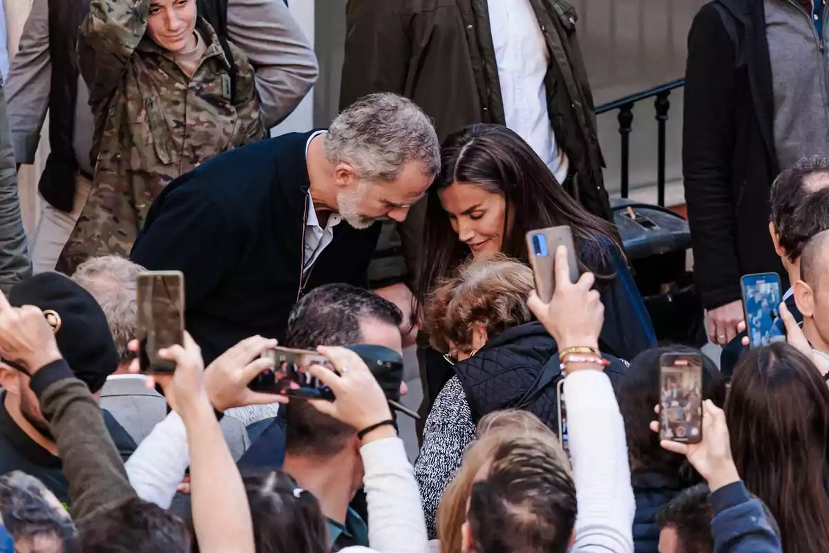 Una pareja se inclina para saludar a una mujer mayor mientras varias personas alrededor toman fotos con sus teléfonos móviles Una pareja se inclina para saludar a una mujer mayor mientras varias personas alrededor toman fotos con sus teléfonos móviles