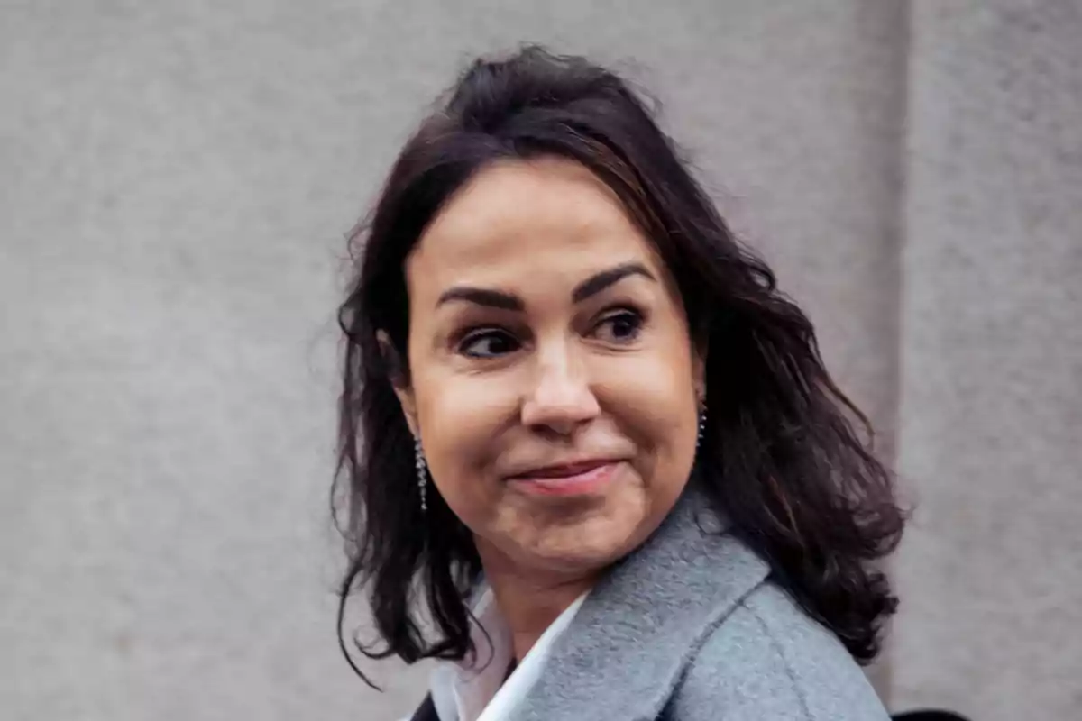 Mujer de cabello oscuro y ondulado con abrigo gris mirando hacia un lado y sonriendo levemente Mujer de cabello oscuro y ondulado con abrigo gris mirando hacia un lado y sonriendo levemente