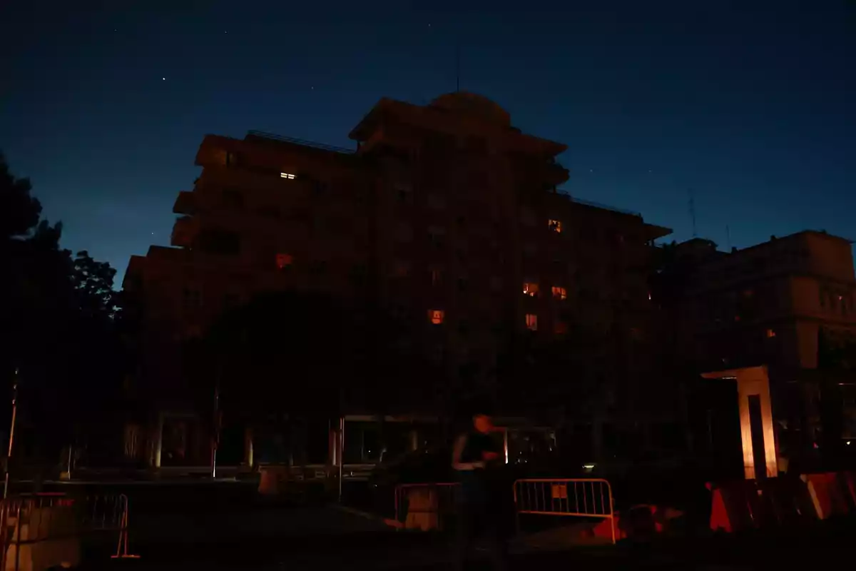 Edificio residencial oscuro con algunas ventanas iluminadas durante la noche y una persona desenfocada caminando al frente