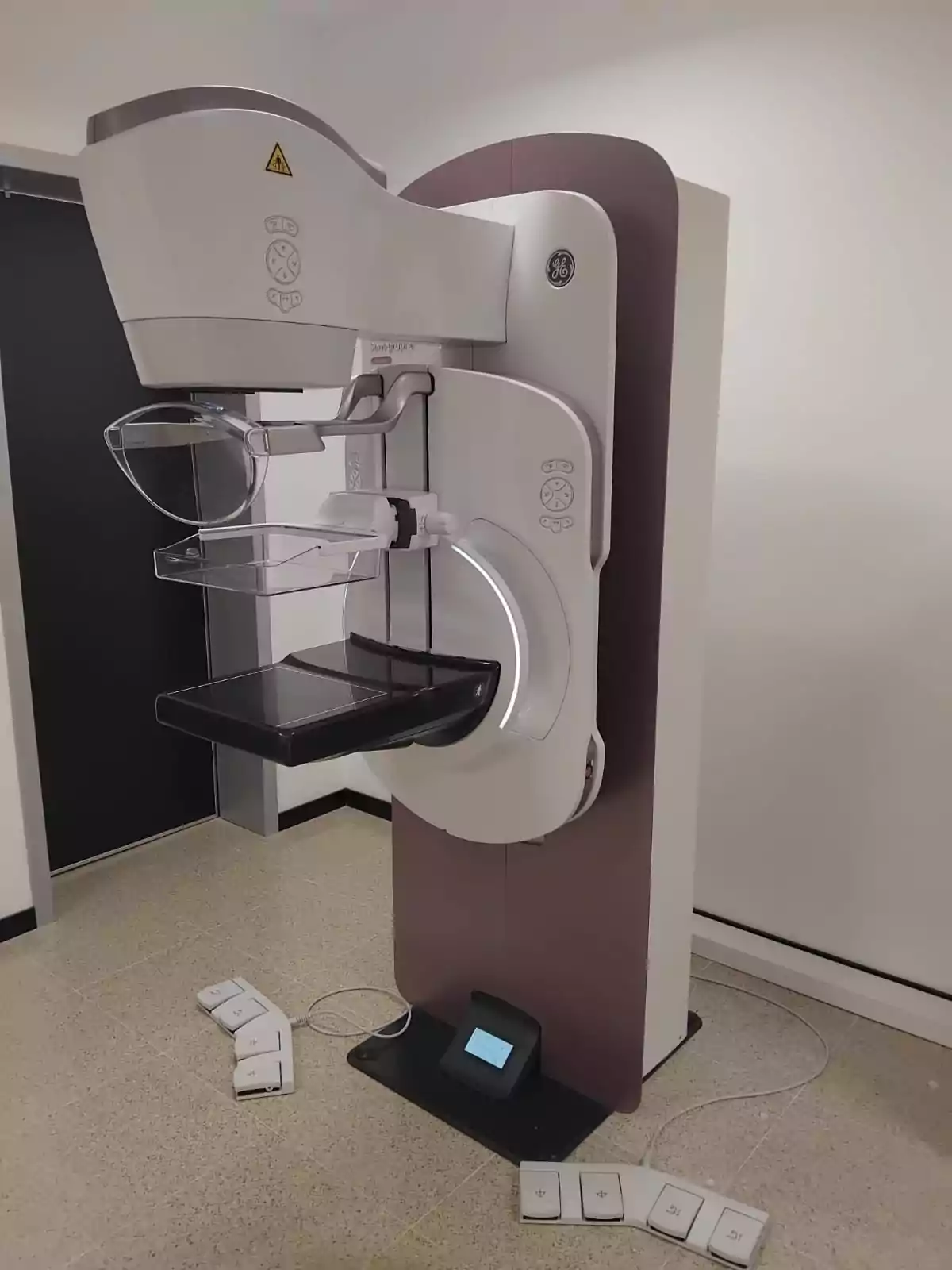 Equipo de mamografía digital en una sala médica con controles en el suelo y paredes blancas de fondo Equipo de mamografía digital en una sala médica con controles en el suelo y paredes blancas de fondo