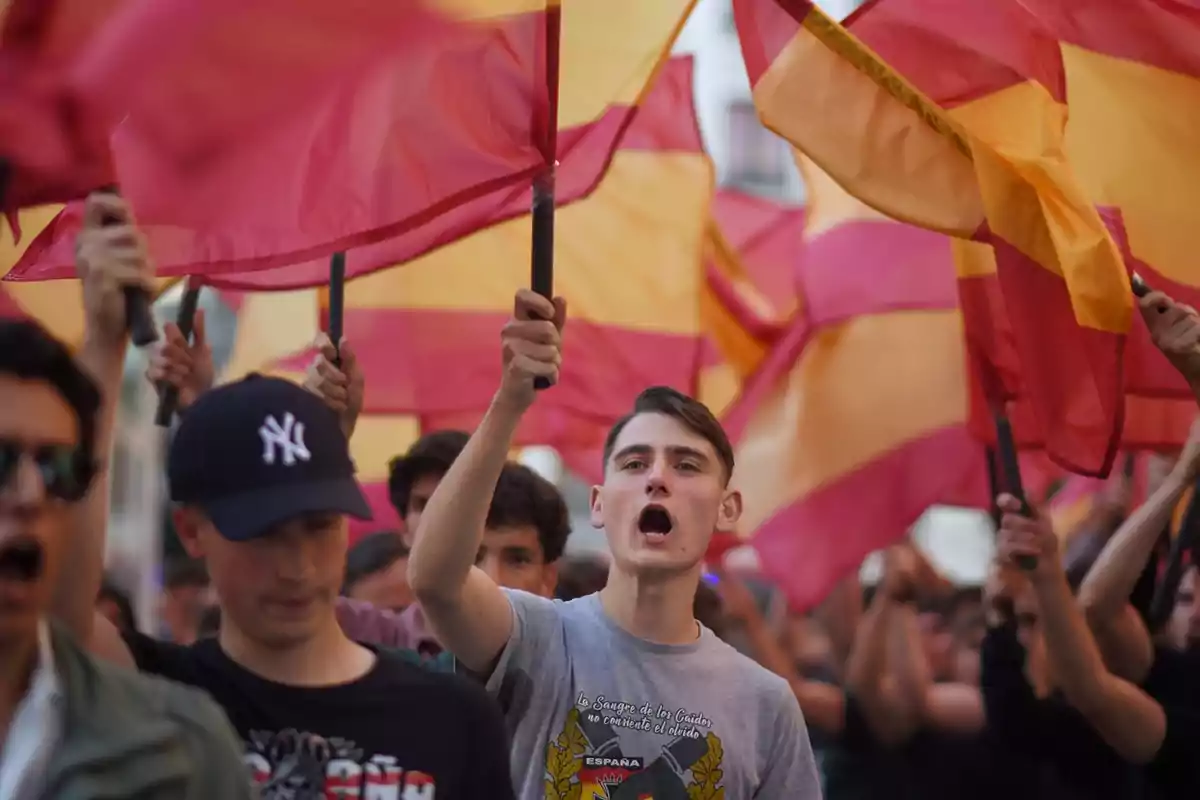 Jóvenes manifestándose con banderas de España mientras gritan y levantan los brazos en una marcha Jóvenes manifestándose con banderas de España mientras gritan y levantan los brazos en una marcha