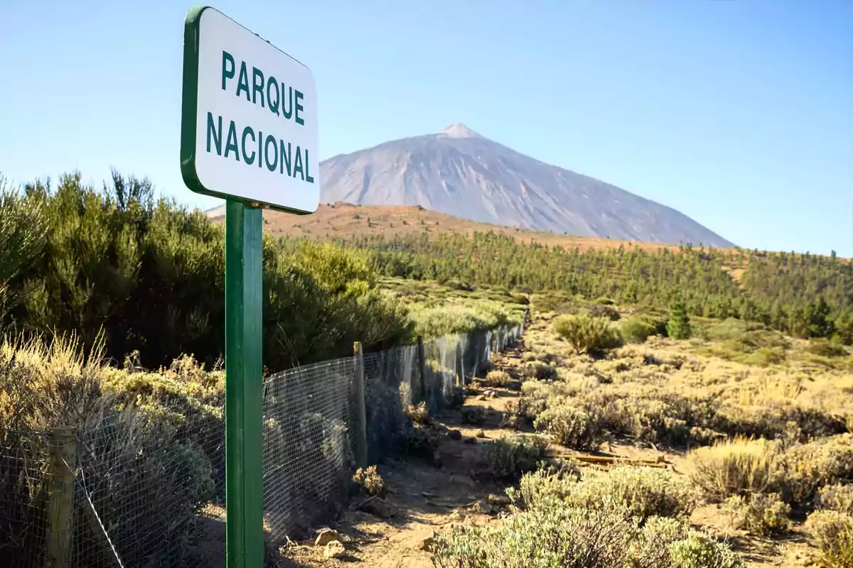Cartel de parque nacional en un entorno natural con vegetación y una montaña al fondo bajo un cielo despejado Cartel de parque nacional en un entorno natural con vegetación y una montaña al fondo bajo un cielo despejado