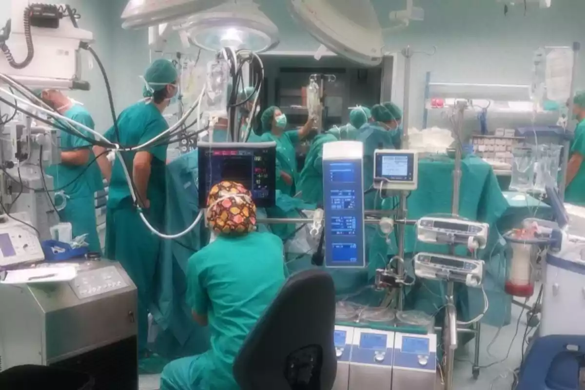 Equipo médico realizando una cirugía en un quirófano con varios monitores y máquinas especializadas mientras el personal usa ropa y gorros quirúrgicos Equipo médico realizando una cirugía en un quirófano con varios monitores y máquinas especializadas mientras el personal usa ropa y gorros quirúrgicos