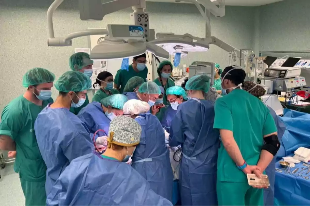 Un grupo de médicos y enfermeros con batas y gorros quirúrgicos realiza una cirugía en un quirófano equipado con luces y equipo médico.