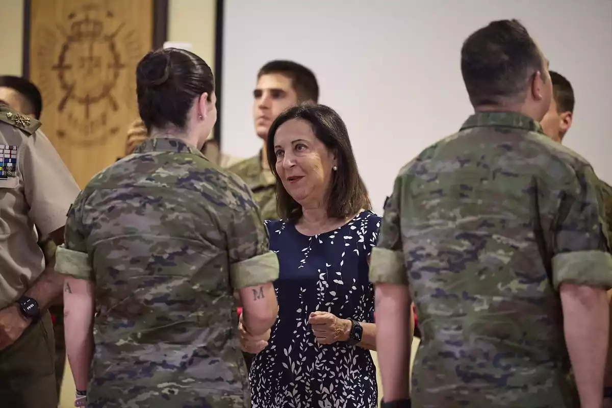 Una mujer vestida de azul con estampado blanco conversa y sonríe mientras saluda a militares con uniforme de camuflaje en un ambiente interior Una mujer vestida de azul con estampado blanco conversa y sonríe mientras saluda a militares con uniforme de camuflaje en un ambiente interior