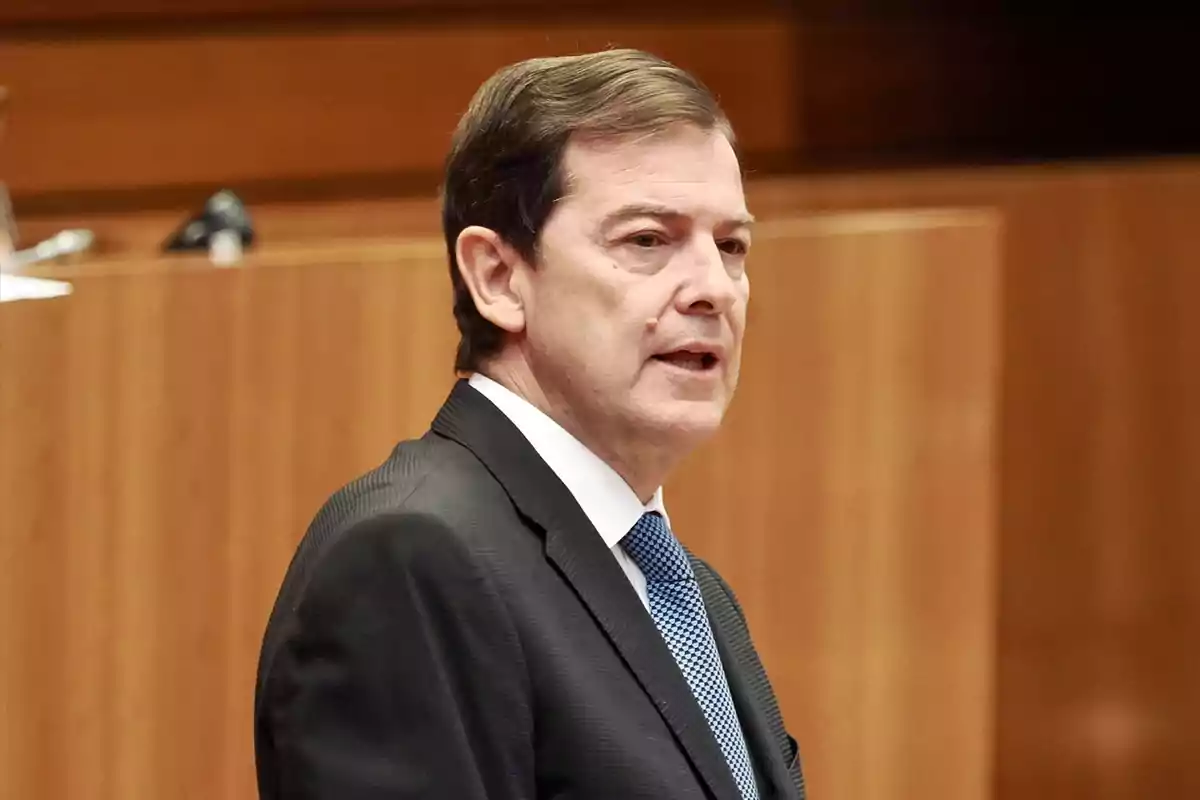 Hombre de mediana edad con cabello corto y traje oscuro hablando en un entorno formal de madera Hombre de mediana edad con cabello corto y traje oscuro hablando en un entorno formal de madera